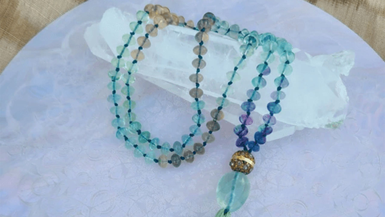 Fluorite gemstone mala prayer bead necklace resting on a quartz crystal