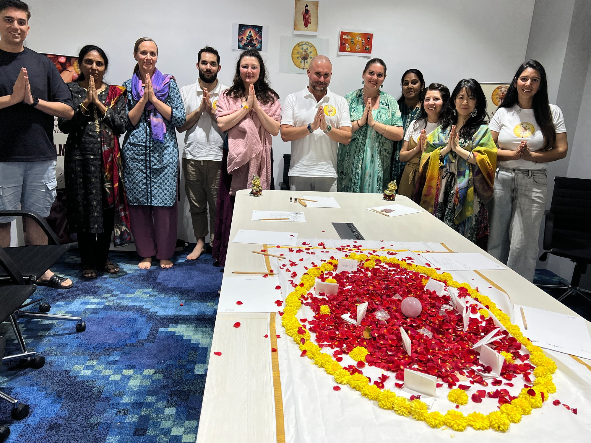 Mypalmleaf group standing in namaste behind a red and yellow flower mandala