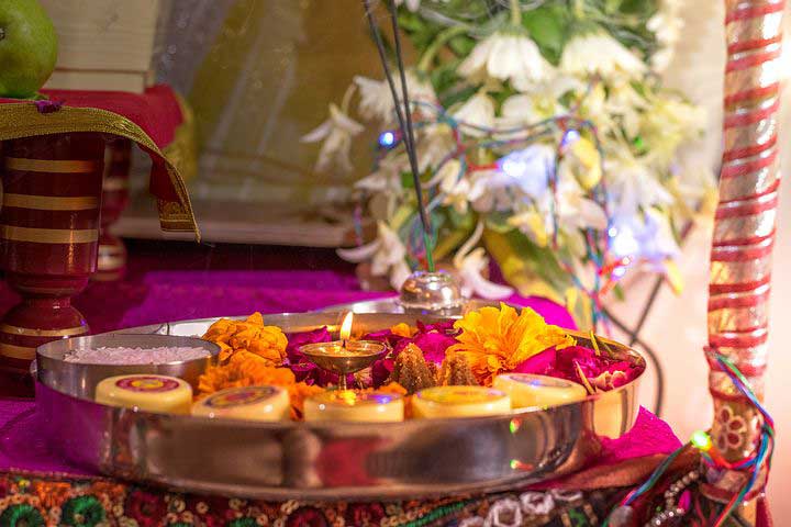 Hindu puja thali with a lit oil lamp and marigold petals on an altar