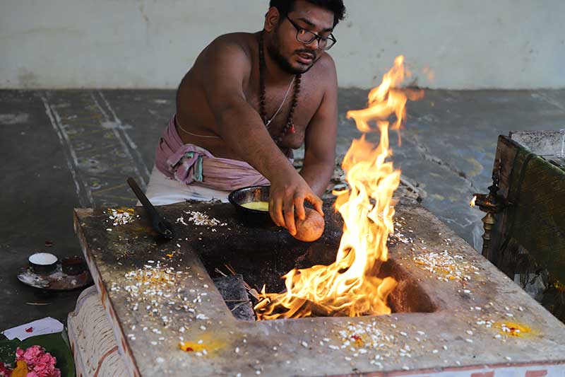 Priest pouring an offering into the sacred fire during a homa ceremony