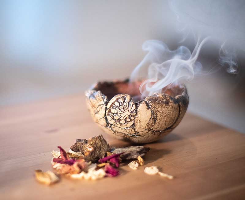 Smoking incense resin in a clay bowl beside dried herbs