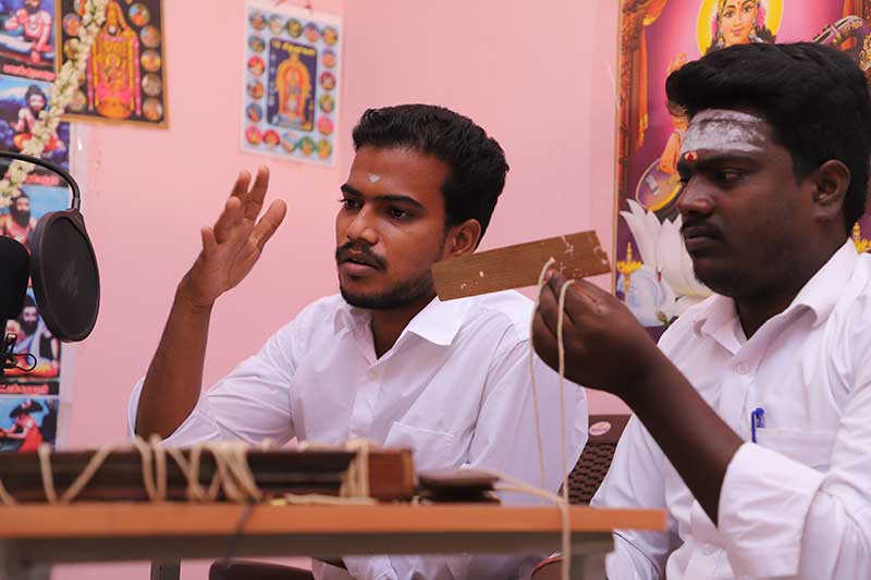Nadi readers discussing a palm leaf manuscript at a recording desk