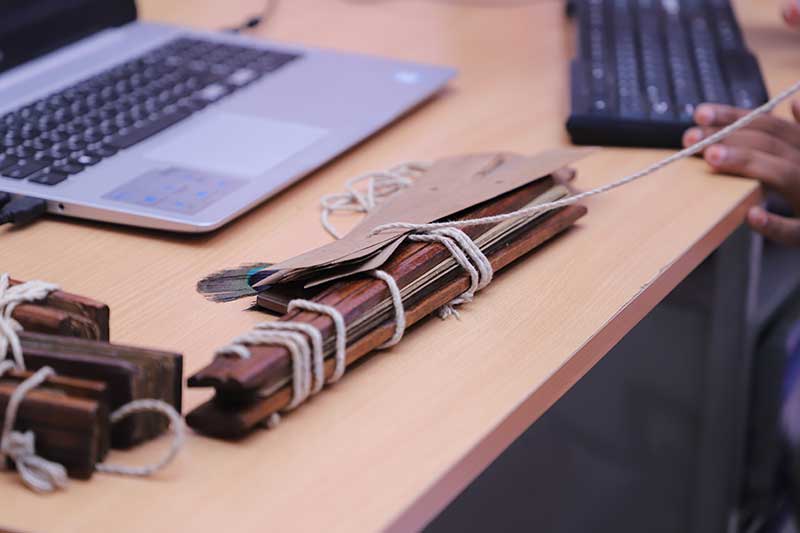Cord-bound palm leaf manuscript bundles beside a laptop on a desk