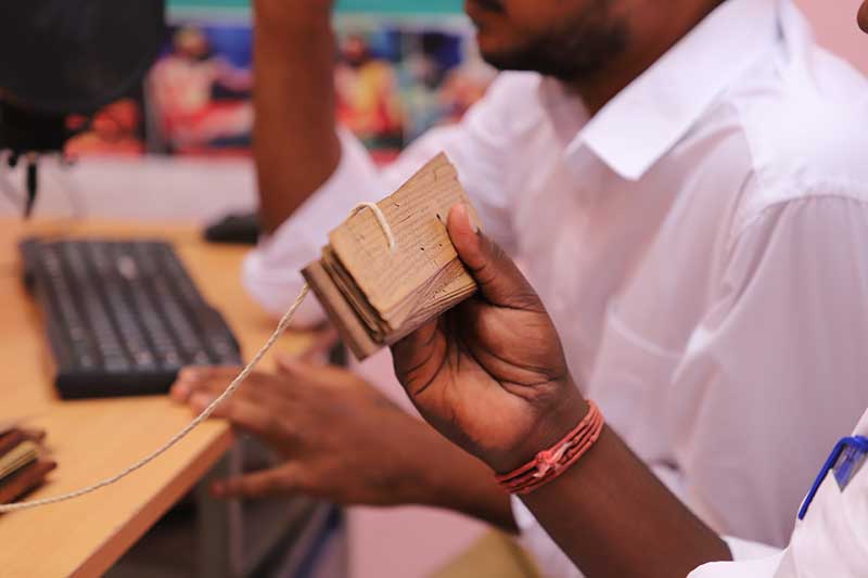 Nadi reader holding a palm leaf manuscript book at his desk