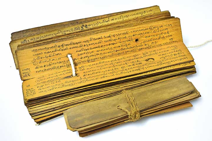 Opened ancient palm leaf manuscript beside a cord-tied bundle
