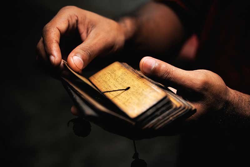Hands cradling a small ancient palm leaf manuscript in the dark