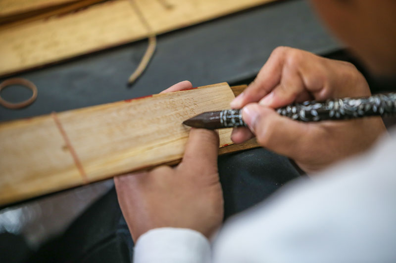 Hand inscribing text onto a palm leaf with a metal stylus