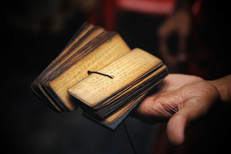 Hand holding a small fanned-open ancient palm leaf manuscript