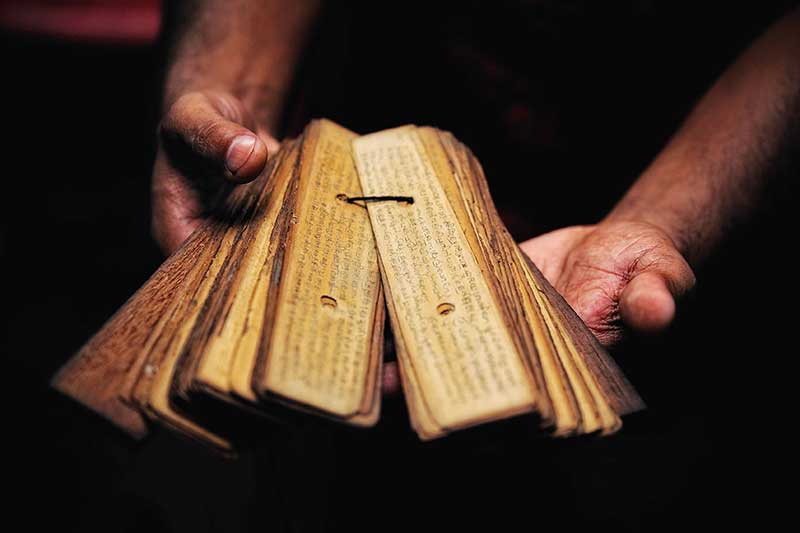 Hands holding a fanned-open bundle of ancient palm leaf manuscripts