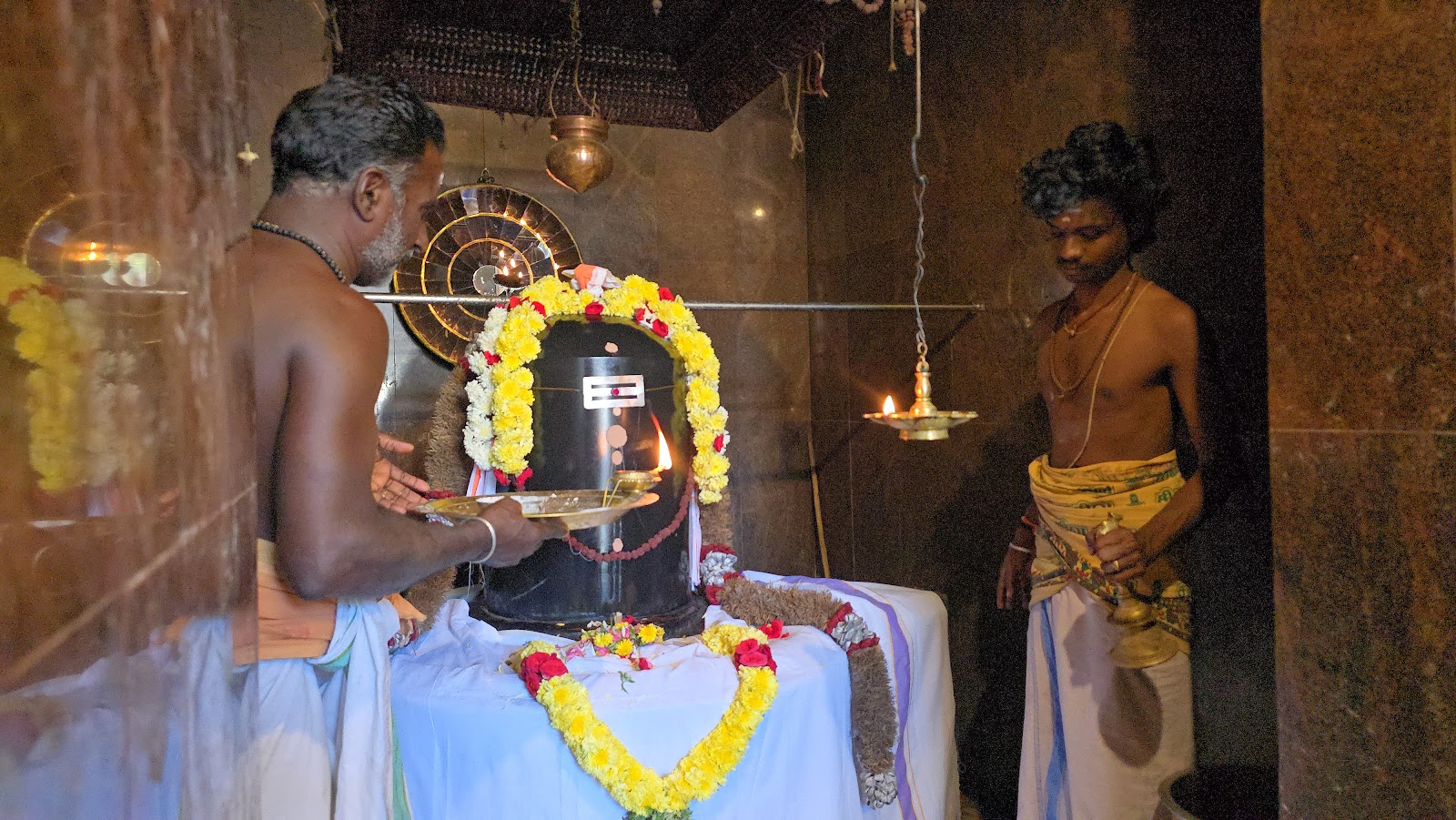 Priest performing abhishekam on a garlanded Shiva lingam