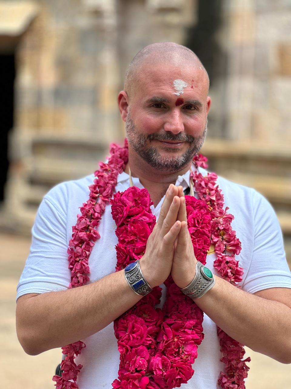 Man with a rose garland greeting with namaste at a South Indian temple