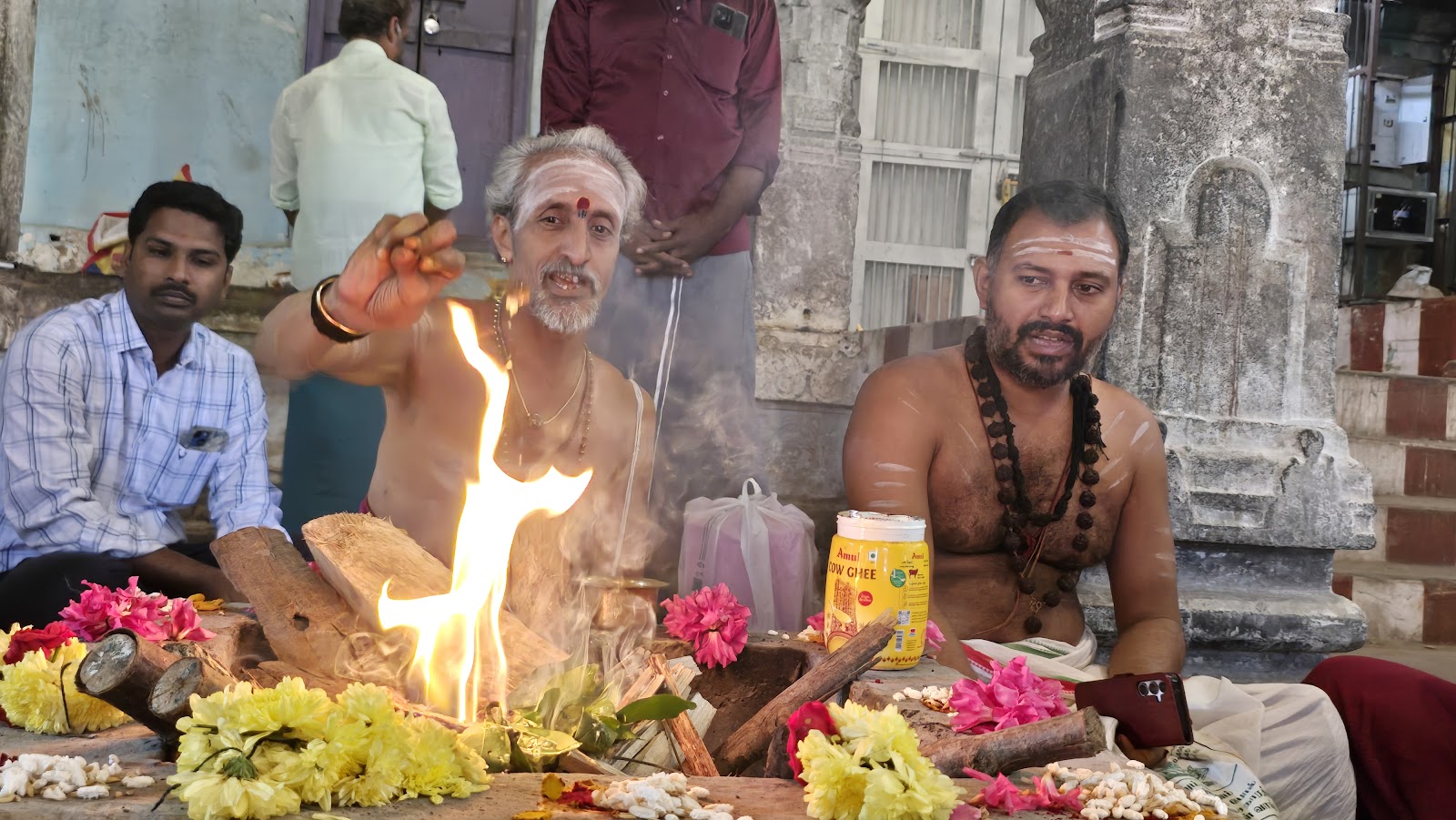 Temple priests performing a homa fire ritual surrounded by flower offerings