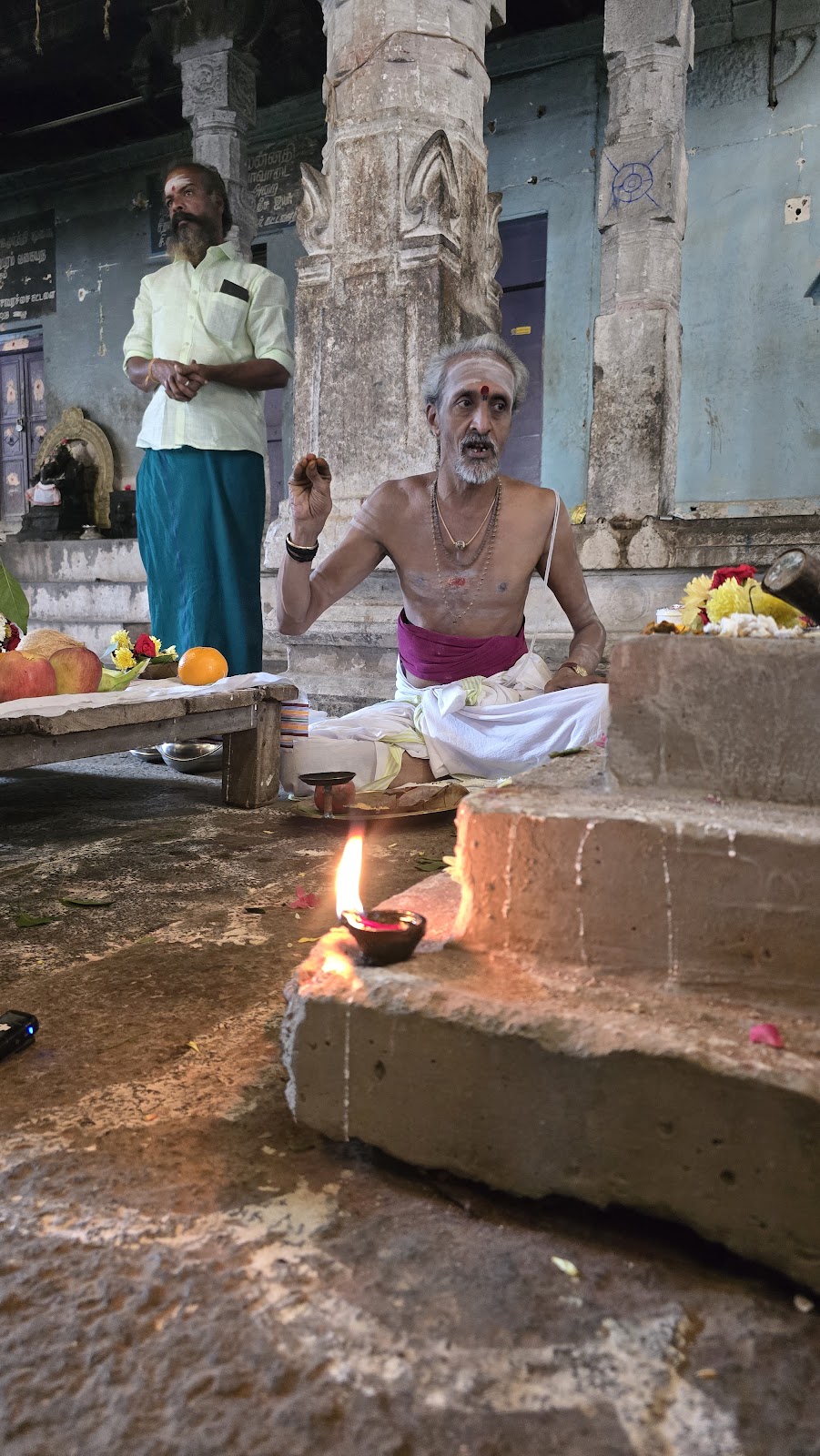 Elderly priest performing a puja with an oil lamp on a temple floor