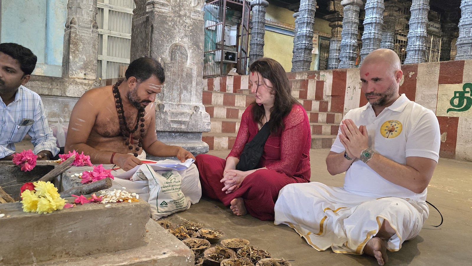 Nadi reader reading a palm leaf manuscript to a seated couple at a temple