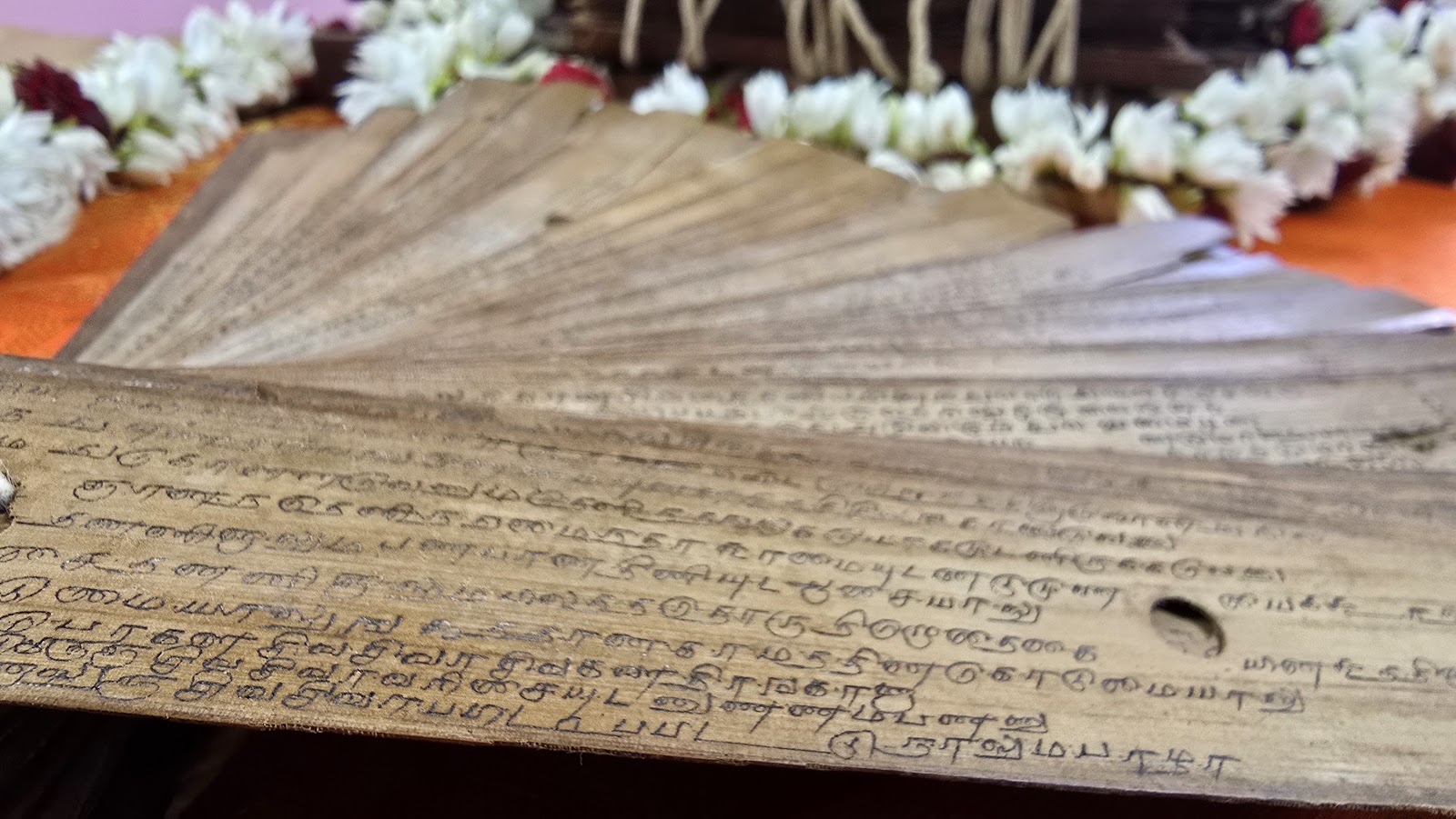 Close-up of a Tamil-inscribed palm leaf manuscript beside a jasmine garland