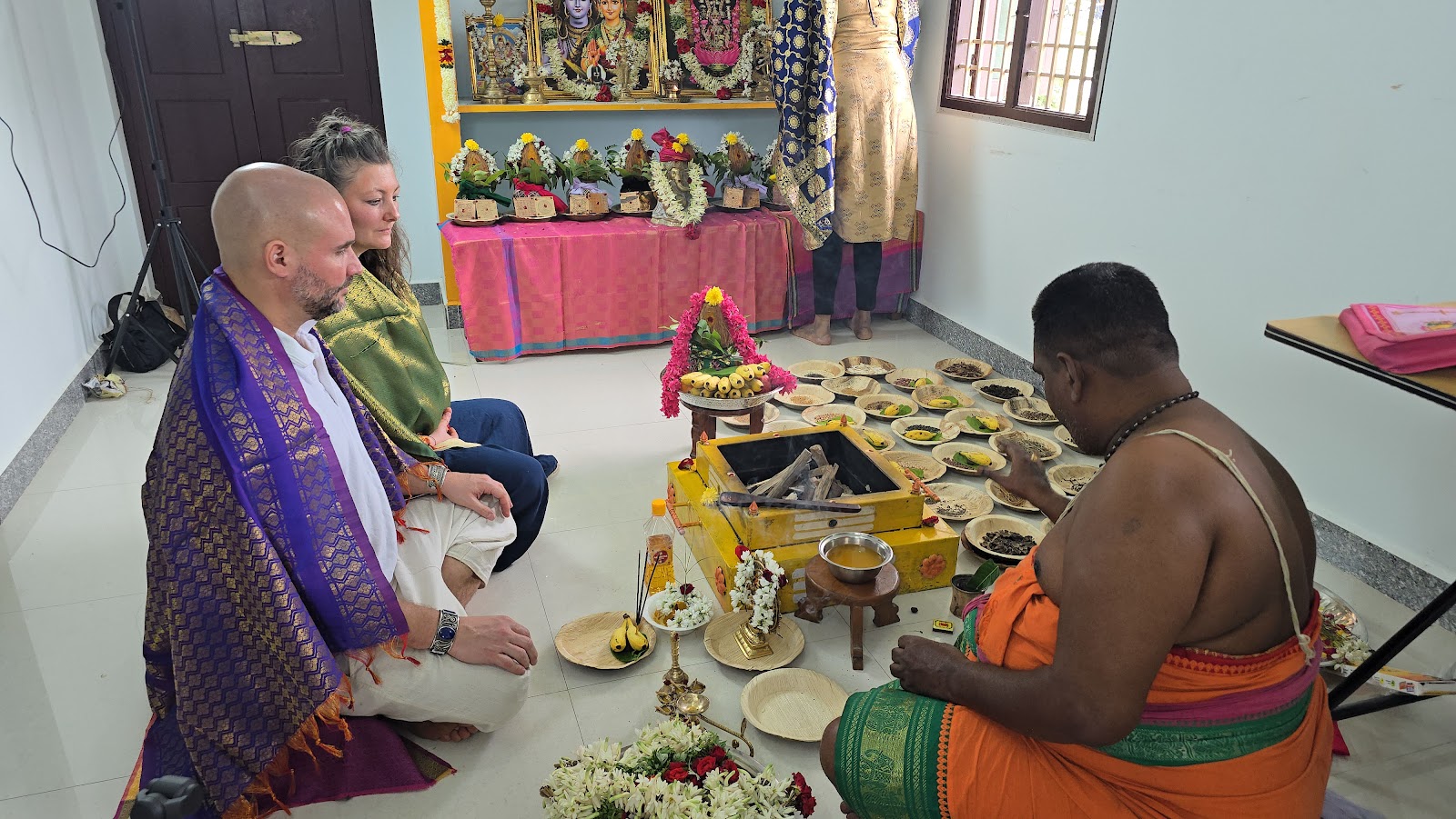 Couple kneeling before a priest during a home fire ritual with offerings