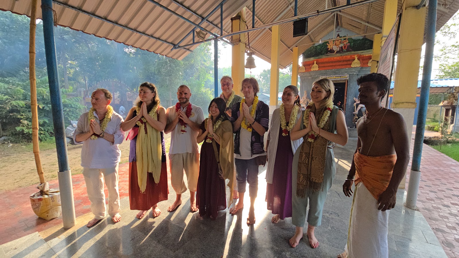 Mypalmleaf group in garlands greeting with namaste at a smoky temple