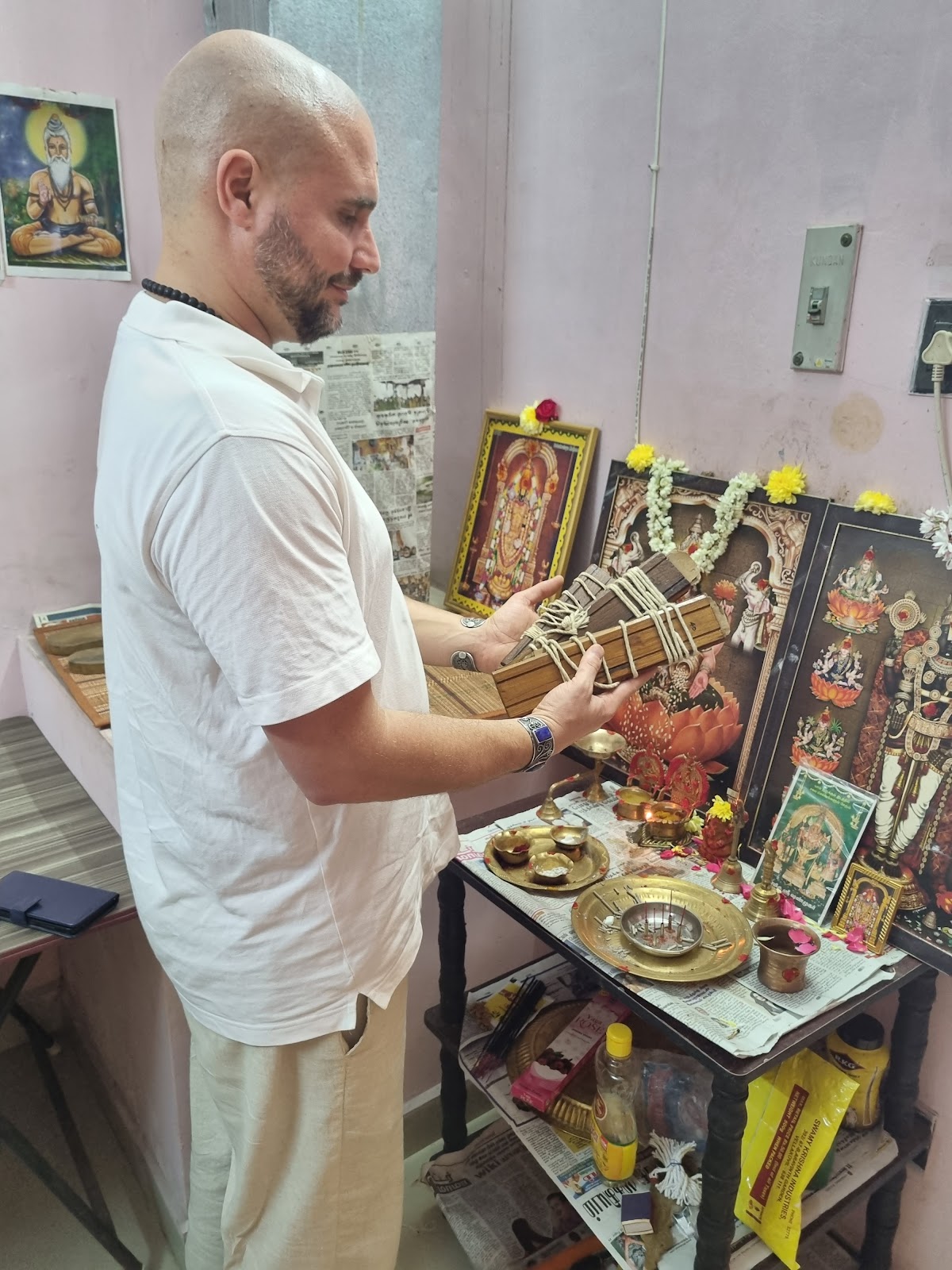 Mypalmleaf host holding a palm leaf manuscript bundle at a Hindu altar